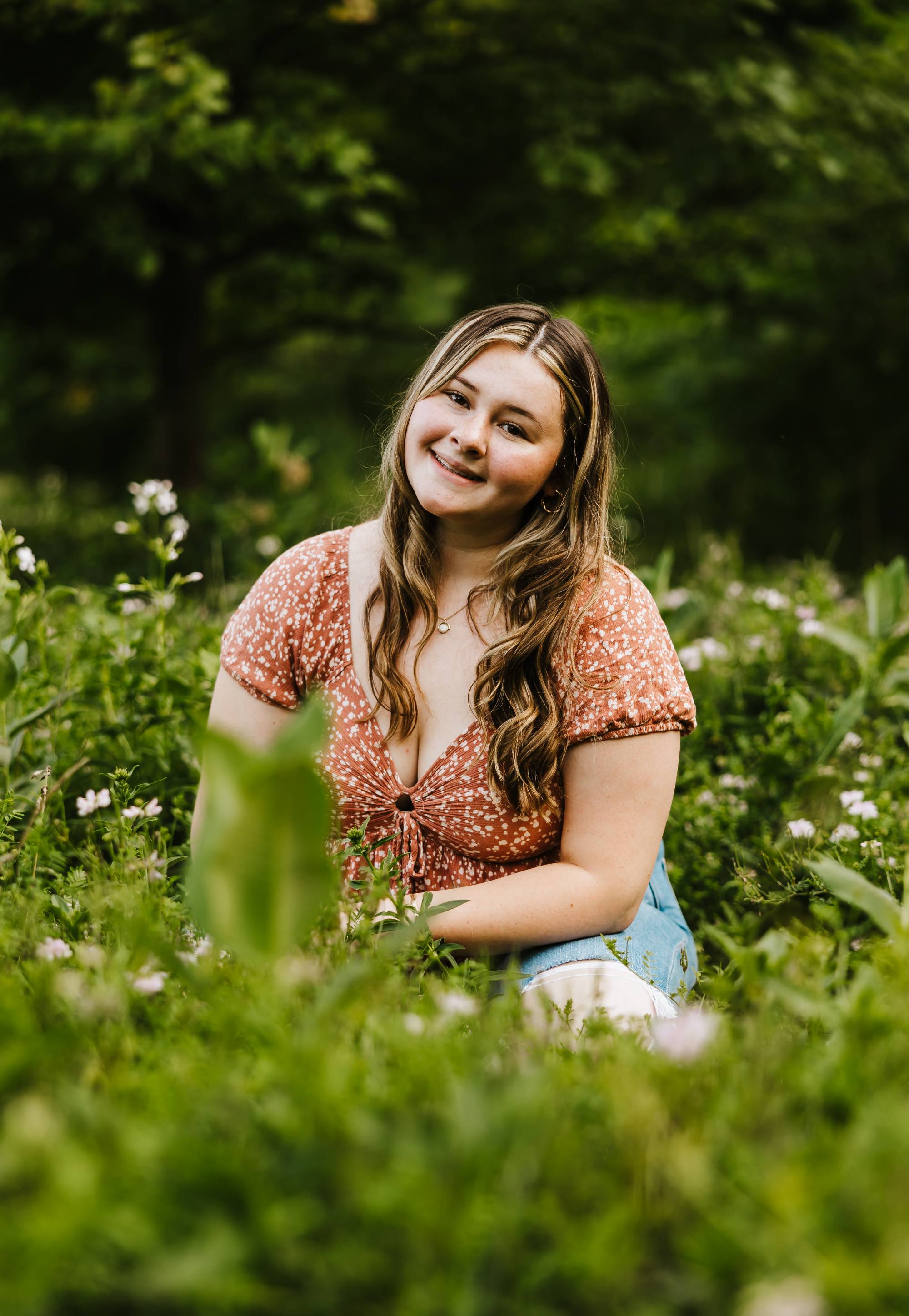 Girl sitting in a green field with a peach floral shirt and curly light brown hair